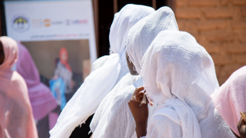 Women in white headscarves are seen from behind, looking towards a large sign with a woman and a UNFPA logo on it