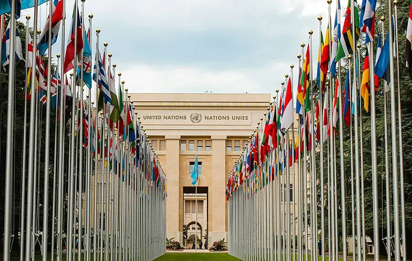 A large grand building with a long green path to it's entrance flanked with flags either side of the path
